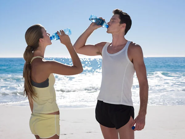 在海滩上喝了几瓶水的年轻夫妇 — 图库照片