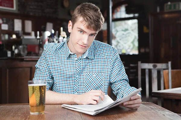 Young man in bar with newspaper and beer