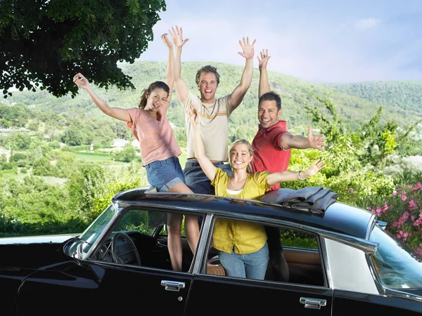 Four friends waving out of car