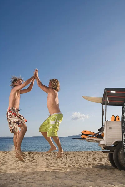 Young men at beach jump by beach — Stock Photo, Image