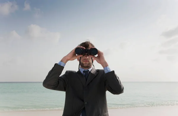 Empresário usando binóculos na praia — Fotografia de Stock