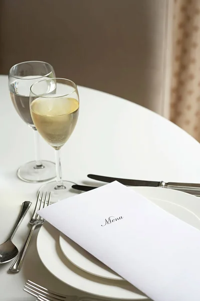 Glass of white wine and a menu on a table — ストック写真
