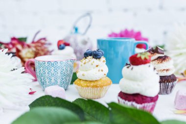 Taze çilek çiçekler ve yapraklar, bir fincan çay ya da kahve ve bir su ısıtıcısı ile cupcakes.