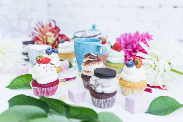 Taze çilek çiçekler ve yapraklar, bir fincan çay ya da kahve ile çeşitli cupcakes.
