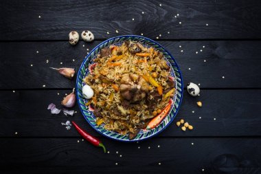 Pilaf and ingredients on plate with oriental ornament on a dark wooden background. Central-Asian cuisine - Plov Top view clipart