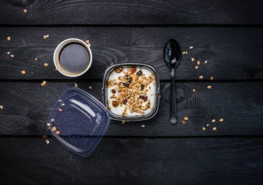 Yoğurtlu müsli ve kahve tek kullanımlık bir kap içinde. Üstten Görünüm koyu ahşap arka plan