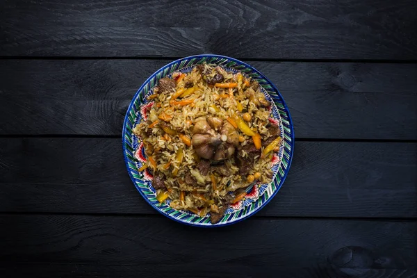 Pilaf on plate with oriental ornament on a wooden background. Central-Asian cuisine - Plov. Top view — Stock Photo, Image