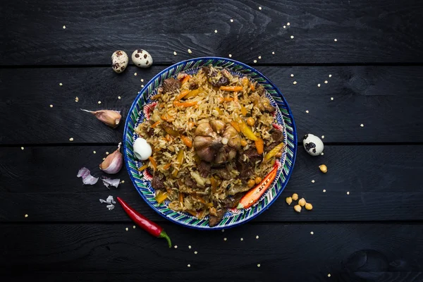 Pilaf e ingredientes na chapa com ornamento oriental em um fundo de madeira escura. Cozinha centro-asiática - Plov Vista superior — Fotografia de Stock