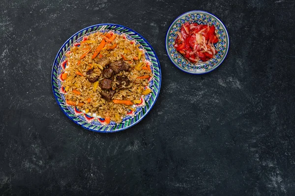 Pilaf y achichuk ensalada en plato con adorno oriental sobre un fondo oscuro. Cocina centroasiática - Plov. Vista superior — Foto de Stock