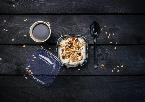 Yoğurtlu müsli ve kahve tek kullanımlık bir kap içinde. Üstten Görünüm koyu ahşap arka plan