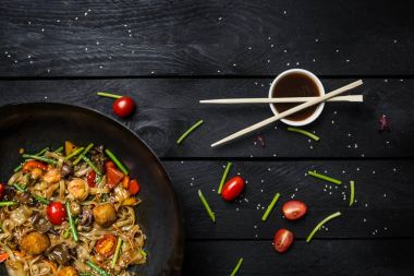 Udon heyecan fry erişte ile deniz ürünleri ve sebze siyah ahşap zemin üzerine wok tavada. Yemek çubukları ve sos ile.