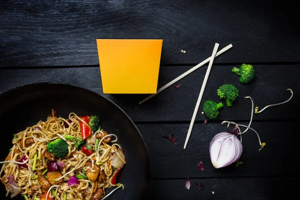 Udon stir fry erişte tavuk ve sebze siyah ahşap zemin üzerine wok tavada. Erişte ile bir kutu