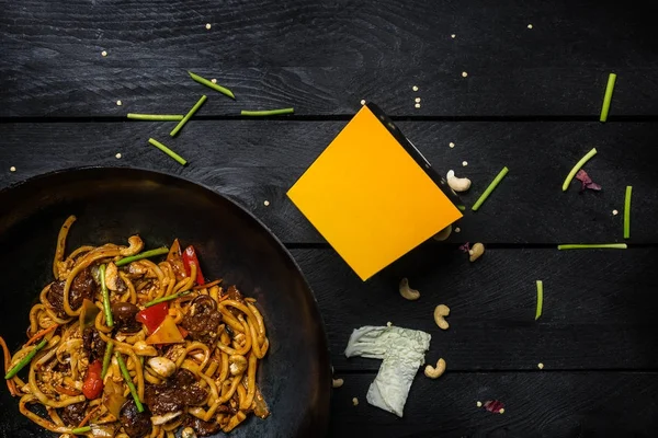 Et ve sebze siyah ahşap zemin üzerine wok tavada ile Udon heyecan fry erişte. Erişte ile bir kutu — Stok fotoğraf