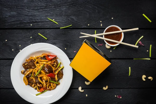 Udon stir fry erişte et ve sebze siyah arka plan üzerine beyaz bir plaka ile. Yemek çubukları ve kutusunu erişte ile — Stok fotoğraf