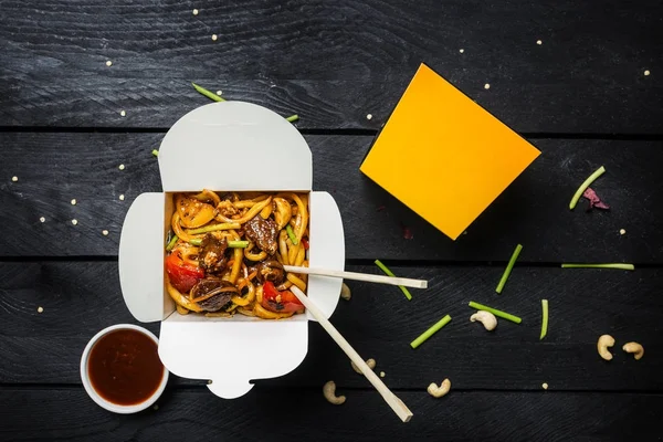 Udon sofríe los fideos con carne y verduras en una caja sobre fondo negro. Con palillos y salsa . —  Fotos de Stock