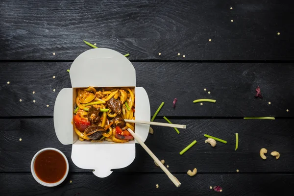 Udon sofríe los fideos con carne y verduras en una caja sobre fondo negro. Con palillos y salsa . —  Fotos de Stock