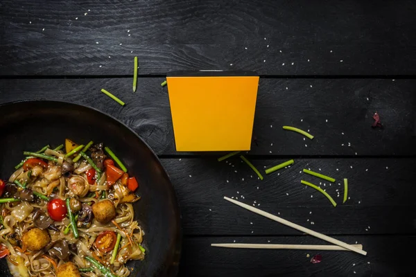 Udon sofríe los fideos con mariscos y verduras en una sartén wok sobre fondo de madera negra. Con una caja para fideos —  Fotos de Stock