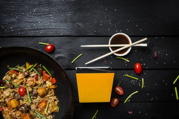 Stir fry nudlích s mořských plodů a zeleniny wok pánvi na černém pozadí dřevěná. Box na nudle — Stock fotografie