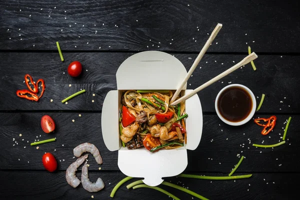 Udon stir fry erişte siyah arka plan üzerine bir kutu içinde deniz ürünleri ile. Yemek çubukları ve sos ile.