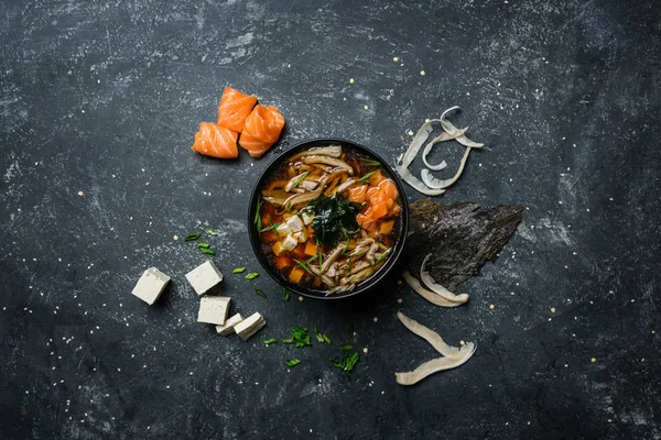 Supă japoneză miso cu tofu și somon într-un castron negru pe un fundal de epocă colorat cu ingrediente. Privire de sus — Fotografie, imagine de stoc