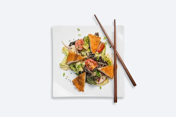 Insalata pan-asiatica, verdure con pollo fritto. Su un piatto quadrato bianco con bacchette su fondo bianco. Vista dall'alto — Foto Stock