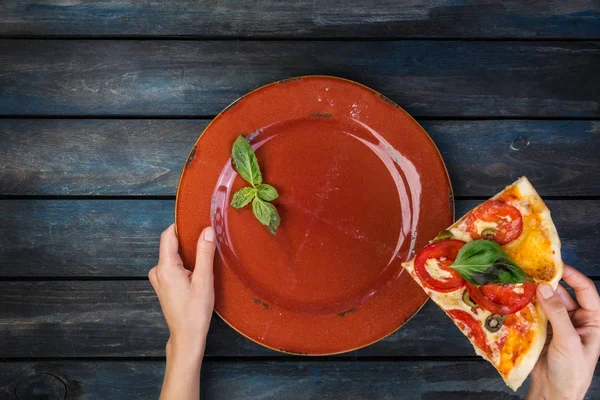 Женские руки держат тарелку с кусочками пиццы Маргарита с томатными ломтиками, оливками и листьями базилика. Вид сверху — стоковое фото