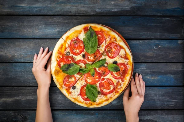 Женские руки и идеальная пицца Маргарита с томатными ломтиками, оливками и листьями базилика. Вид сверху . — стоковое фото