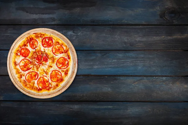 Пицца Маргарита на деревянном подставке с томатными ломтиками на темном деревянном фоне. Ориентация сверху с левой стороны — стоковое фото