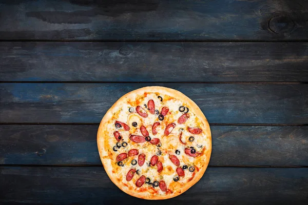 Pizza deliciosa com salsicha defumada e azeitonas em um fundo de madeira escura. Visão superior orientação inferior — Fotografia de Stock
