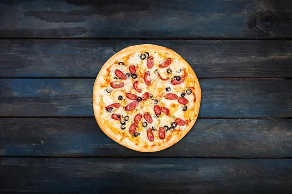 Pizza deliciosa com salsicha defumada e azeitonas em um fundo de madeira escura. Visão superior orientação centro — Fotografia de Stock