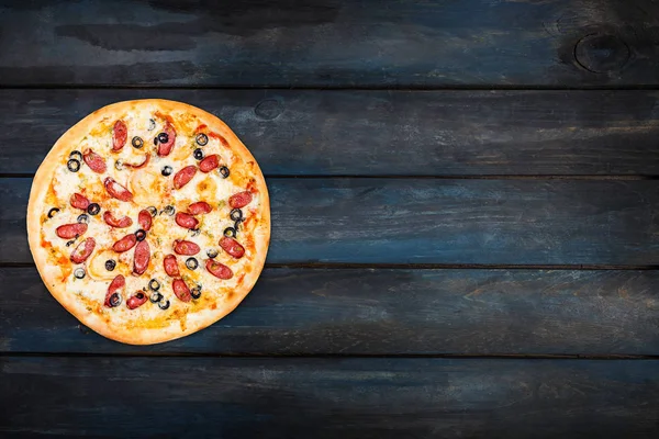 Вкусная пицца с копченой колбасой и оливками на темном деревянном фоне. Ориентация сверху с левой стороны — стоковое фото