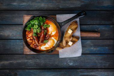 Sıcak bir tavada kızarmış yumurta, sosis, fasulye, yeşil ve tost ile üzerinde Servis Kahvaltı. Renkli ahşap arka plan üzerinde. Üstten Görünüm