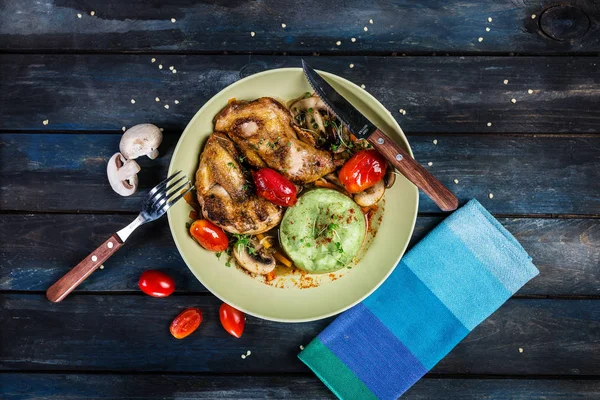 Brathähnchen mit Gemüse und grünem Kartoffelbrei. Gabel, Messer und Serviette auf farbigem Holzgrund. Ansicht von oben — Stockfoto