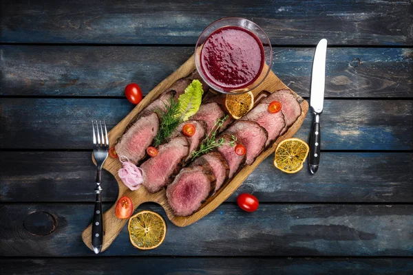 Gegrilltes Roastbeef mit Preiselbeersoße auf Schneidebrett mit Salz und Pfeffer. Ansicht von oben. — Stockfoto