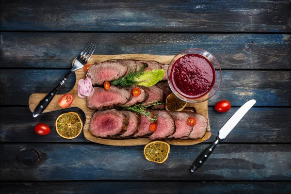 Gegrilltes Roastbeef mit Preiselbeersoße auf Schneidebrett mit Salz und Pfeffer. Ansicht von oben. — Stockfoto