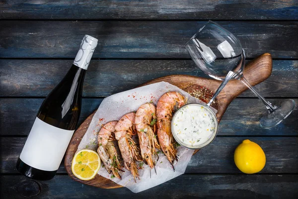 Grandes crevettes ou langoustine avec sauce blanche, bouteille de vin, verre pour le vin et la moitié d'un citron sur une planche en bois. Vue du dessus — Photo