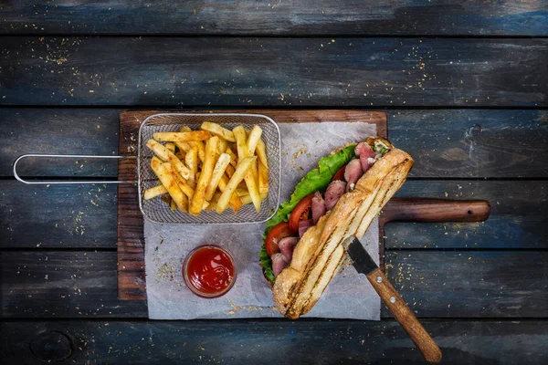 stock image Large bread sandwich with vegetables and roast beef on wooden cutting board