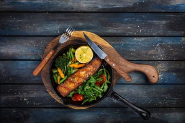 Grilled salmon fillet in a frying pan, vegetables, arugula with a lemon. clipart