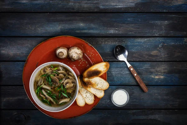 Fresh mushroom soup with green onion sour cream and bread crisps with cutlery. On a ceramic plate. Colored wooden background. Top view — Stock Image Fresh mushroom soup with green onion sour cream and bread crisps with cutlery. On a ceramic plate. Colored wooden background. Top view Stock Image