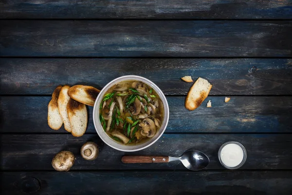 Fresh mushroom soup with green onion sour cream and bread crisps. In white bowl dishe with cutlery. Colored wooden background, spoon. Top view — Stock Image Fresh mushroom soup with green onion sour cream and bread crisps. In white bowl dishe with cutlery. Colored wooden background, spoon. Top view Stock Picture