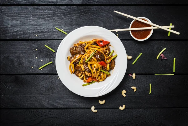 Udon stir fry noodles with meat or chicken and vegetables in a white plate with chopsticks.