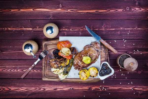 Leckeres Steak vom Grill mit verschiedenen Braten und Mais. Es gibt eine Pfeffermühle, Soße und Besteck. Ansicht von oben — Stockfoto