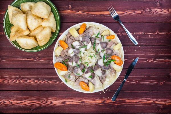 Prato de Beshbarmak com baursak - comida de Cazaquistão asiática tradicional e pão nacional. Macarrão com cordeiro e cebola close-up em um prato na mesa. Vista horizontal superior Imagem De Stock