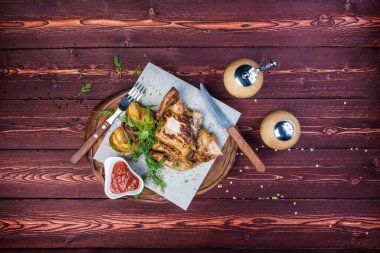 Ahşap arka planda ızgara kızarmış tavuk tütünü. Biber öğütücü ve çatal bıçak takımı var. Üst görünüm