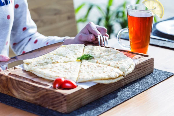 İlahi, peynirli ve patatesli tortilla hamuru, kesme tahtasında. Kadın eli ve bir fincan çayla