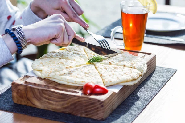 Hychiny, masa de tortilla con queso y patatas, en la tabla de cortar. Con manos femeninas y una taza de té — Foto de Stock