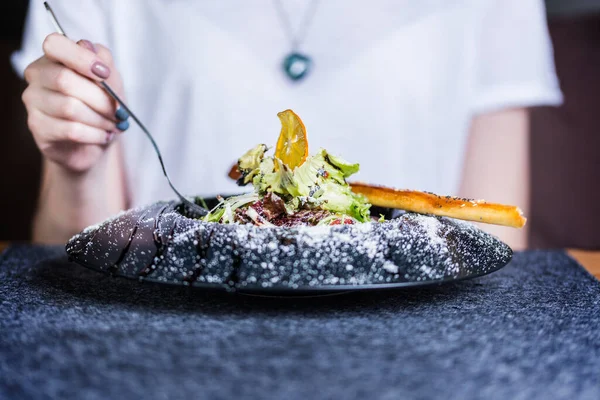 Mulher está comendo almoço saudável em fundo escuro. Salada com queijo parmesão Imagem De Stock