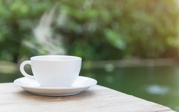 Xícara de café na mesa de madeira com fundo lagoa verde — Fotografia de Stock