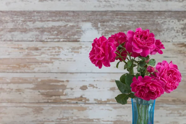 Stilleven met roze rozen bloemen in blauwe vaas op grunge houten — Stockfoto