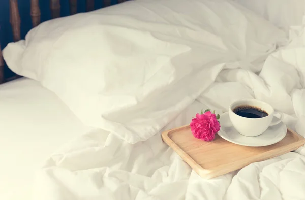 Tasse Kaffee und rosa Rosenblume mit Holztablett auf Bettrücken — Stockfoto